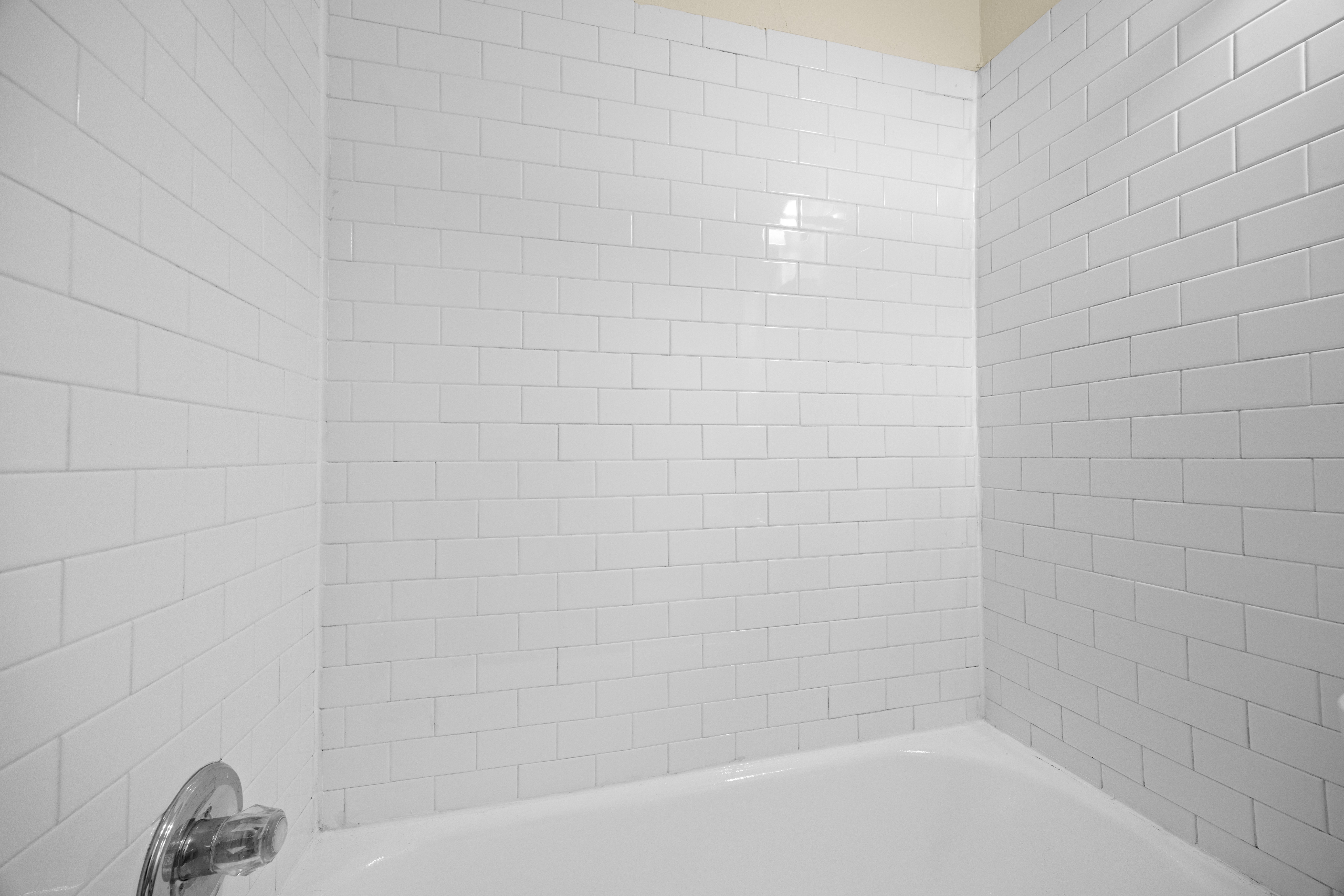 A white tiled bathroom with a white bathtub and faucet.
